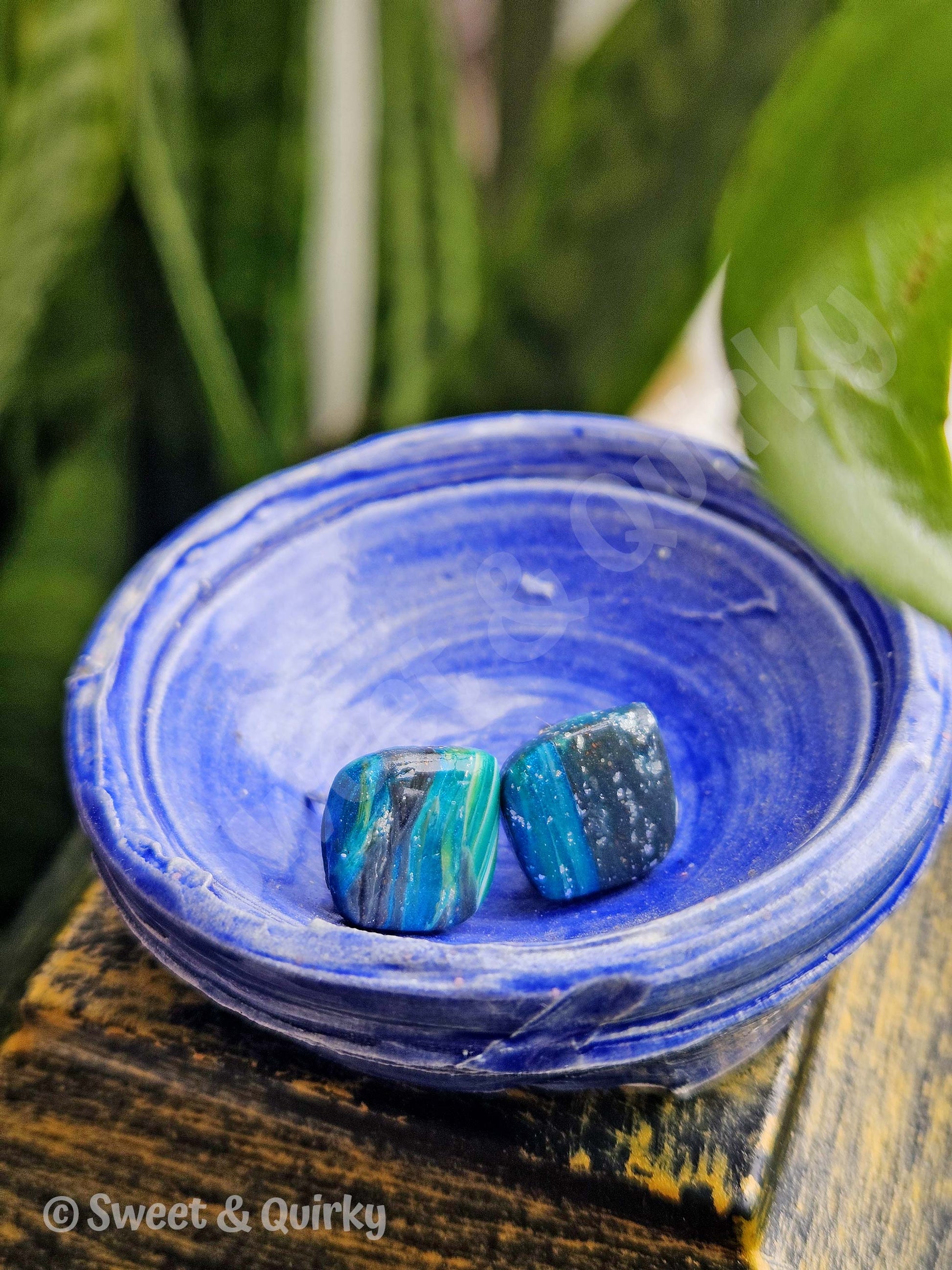 Blue agate faux stones in a matching blue dish on a wooden surface with green plants in the background.