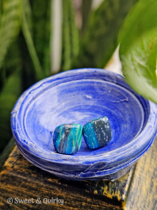 Blue agate faux stones in a matching blue dish on a wooden surface with green plants in the background.