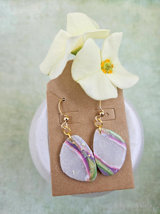Pair of earrings on a brown card with white flowers in the background
