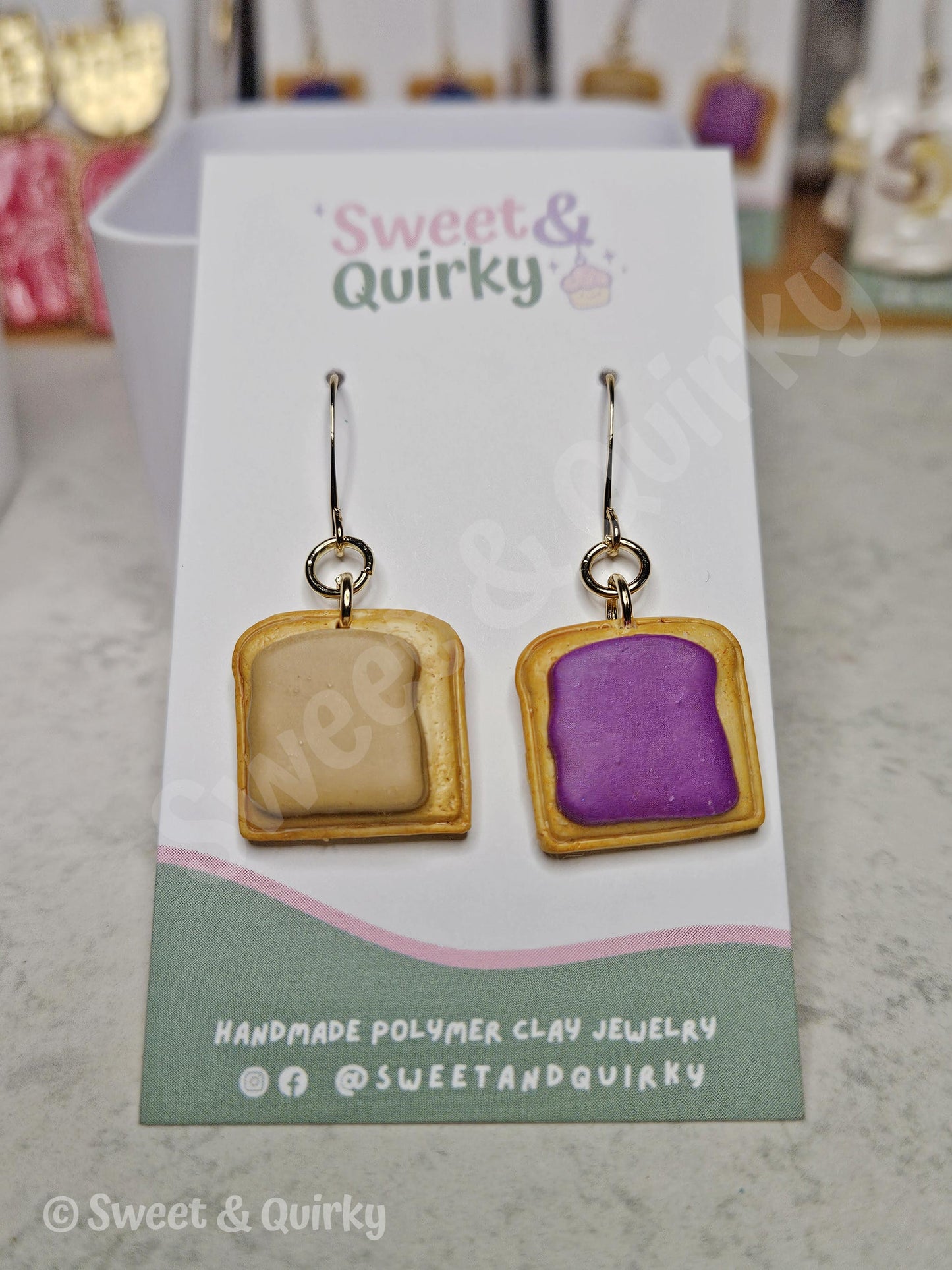 Pair of peanut butter and grape jelly earrings on a 'Sweet & Quirky' branded card with a purple and gold design.