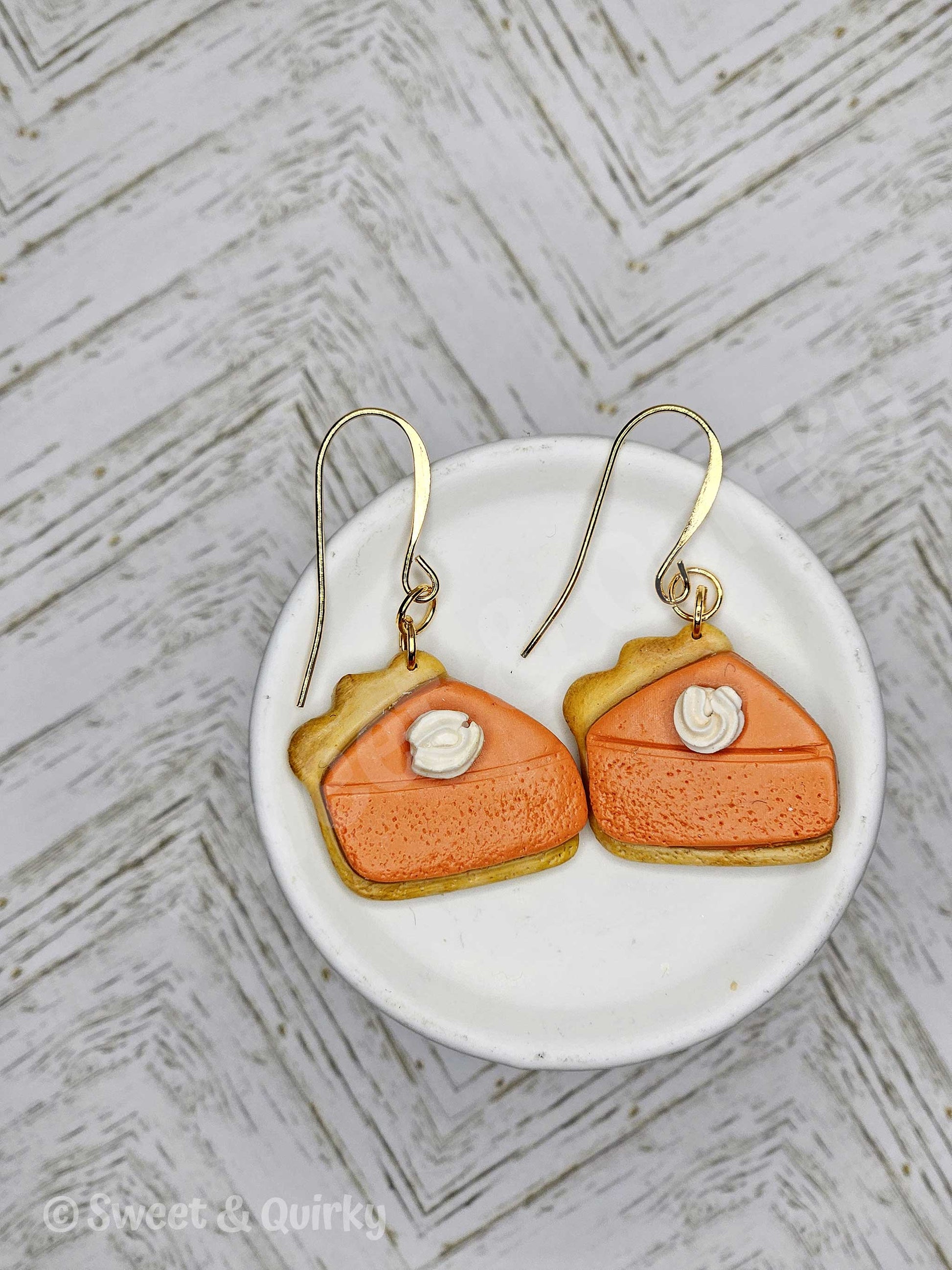Pumpkin pie shaped earrings on a white dish with a textured gray background
