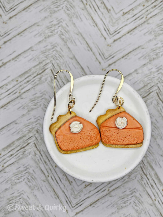 Pumpkin pie shaped earrings on a white dish with a textured gray background