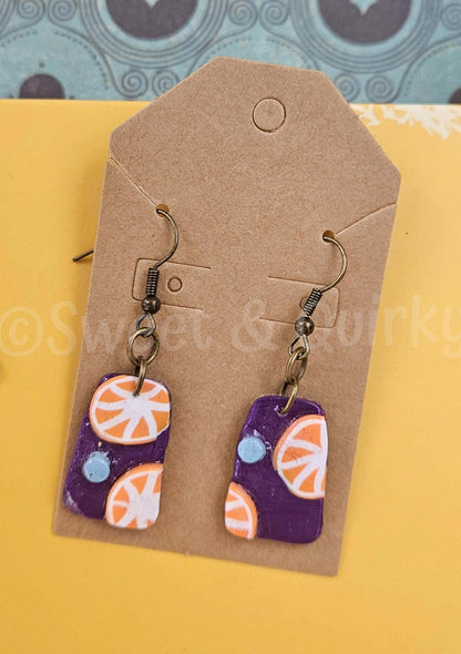 Pair of earrings with orange and purple design on a brown card with 'Sweet & Turkey' branding.