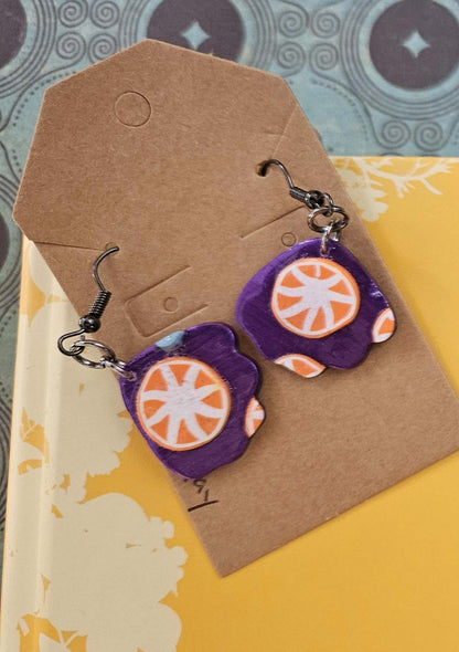 Pair of purple earrings with orange circular designs on a brown card.