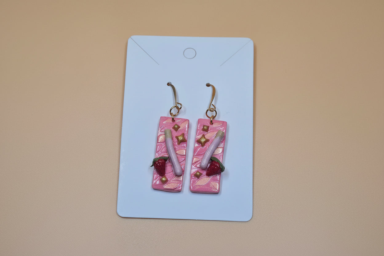Pair of pink earrings with gold accents on a white card against a beige background