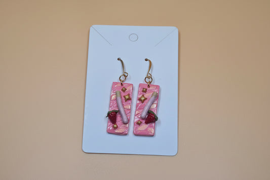 Pair of pink earrings with gold accents on a white card against a beige background