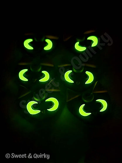 Glowing green crescent moon-shaped eyes on a dark background - Sailor Moon's Luna cat.