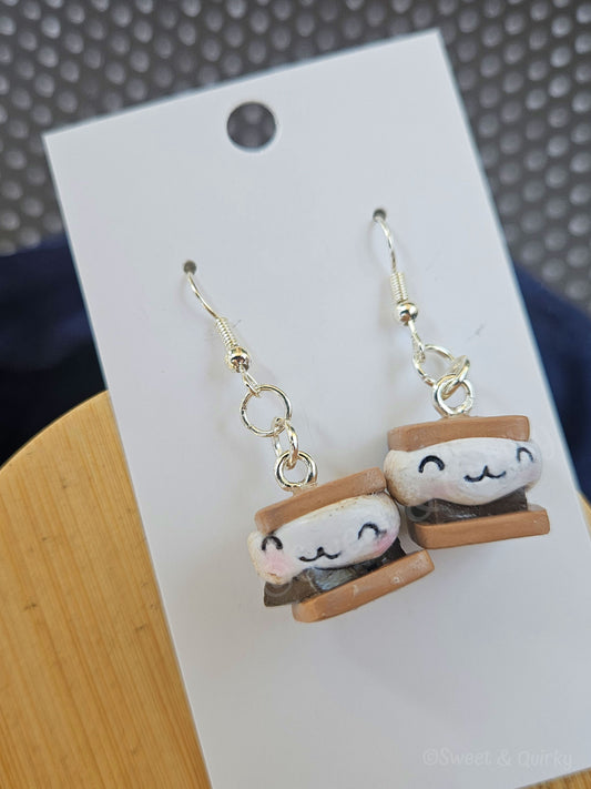 Pair of earrings shaped like cute face s'mores on a white card with a textured background.