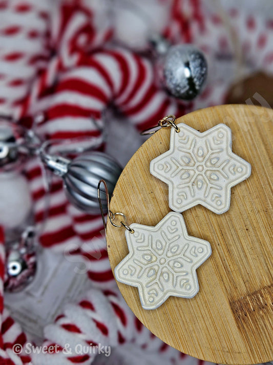 Star-shaped snowflake earrings on a wooden stand with a festive background