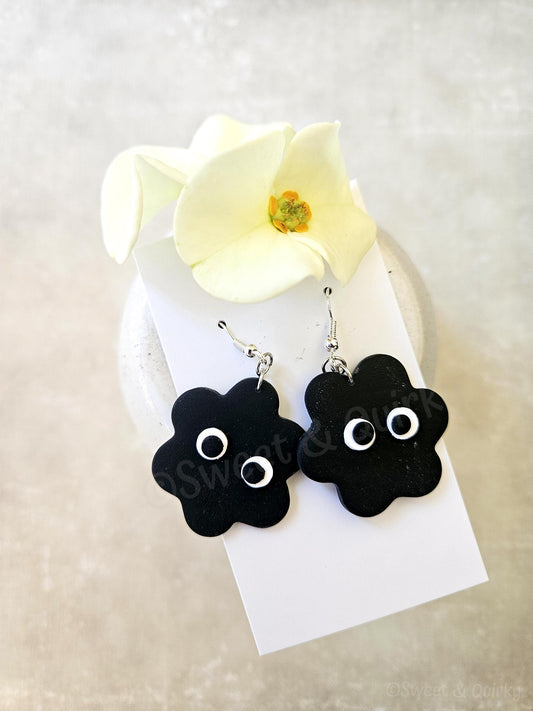 Black flower-shaped earrings with white centers on a card with a white flower.