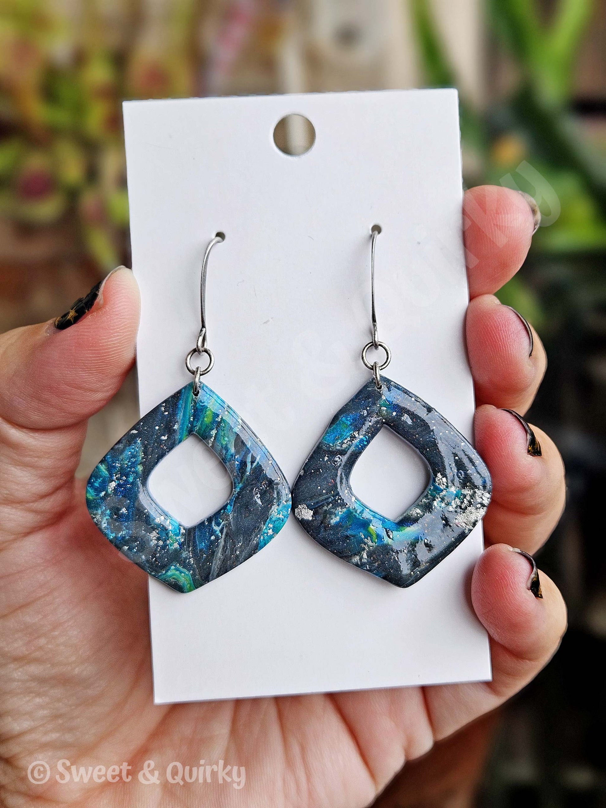 Blue and black marbled earrings on a white card held by a hand.