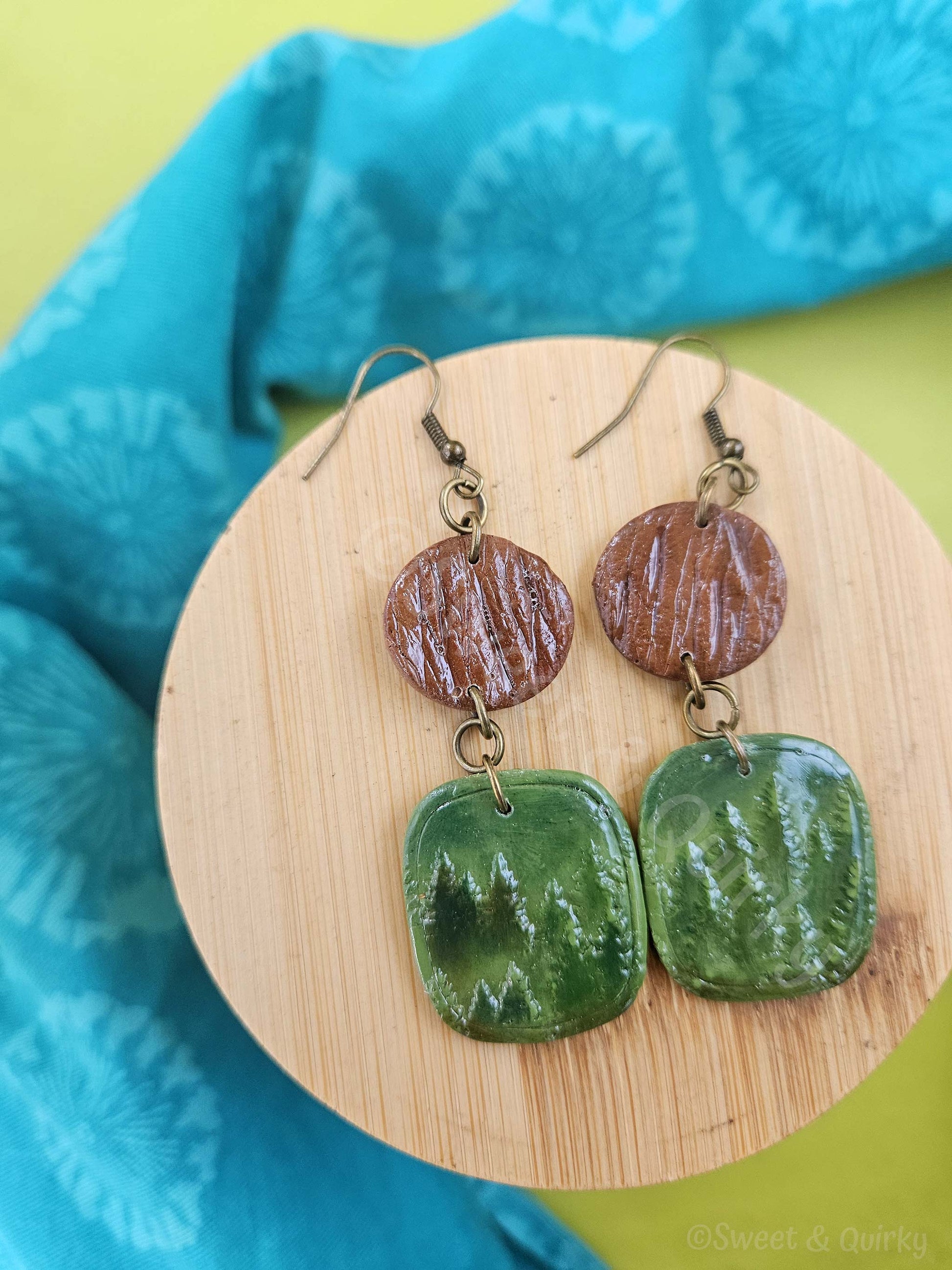 Pair of earrings with brown and green ceramic discs on a wooden stand with a blue fabric background.