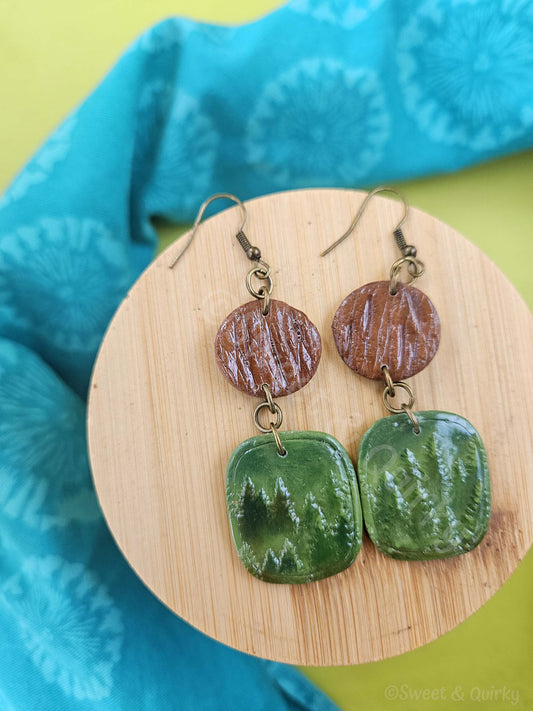 Pair of earrings with brown and green ceramic discs on a wooden stand with a blue fabric background.