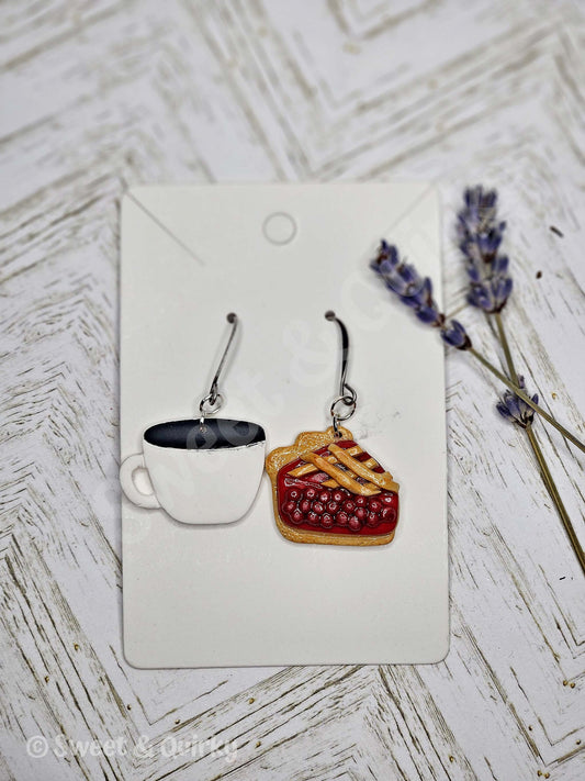 Pair of earrings shaped like a coffee cup and a pie on a white card with lavender flowers in the background.