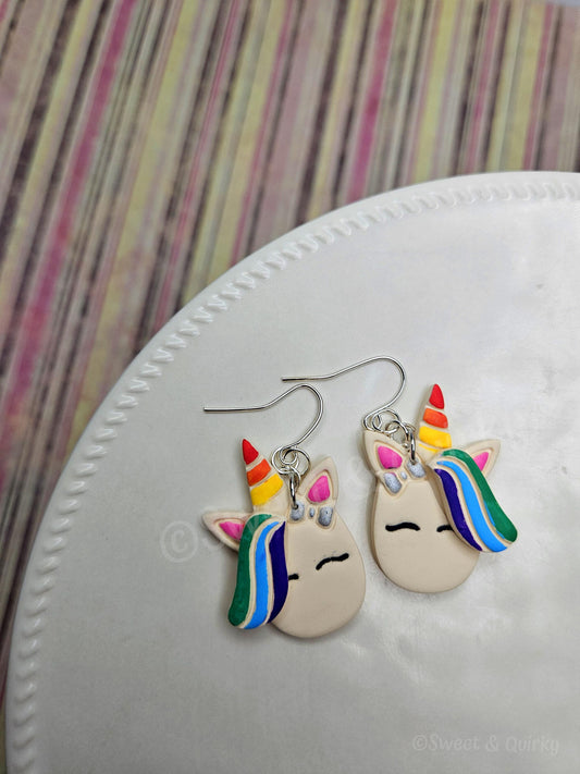 Unicorn-shaped earrings with rainbow colors on a white surface.