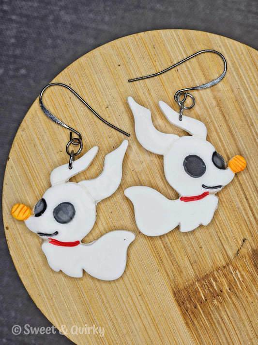 White dog-shaped ghost earrings with black eyes and red collars on a wooden surface, branded 'Sweet & Quirky'.